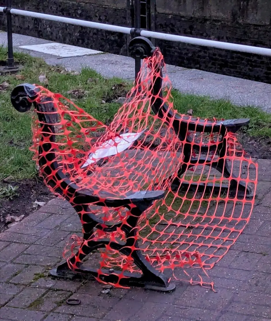 The remains of a bench with no slats, covered in orange safety netting.